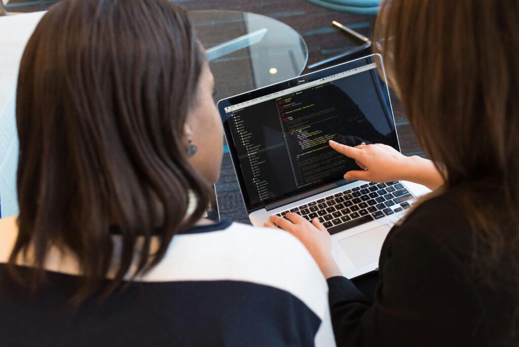 Two women working together on software programming indoors, focusing on code.